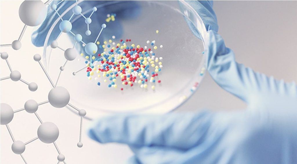 Gloved hands holding colored molecules in a petri dish